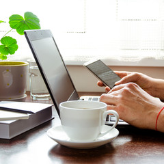 Businessman, freelancer holding pen, using mobile smart phone, working on laptop computer at home