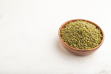 Wooden bowl with raw green mung bean on a white wooden background. Side view, copy space.