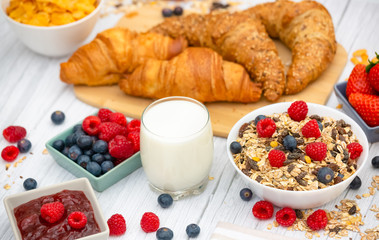 Breakfast Served in the morning with Butter croissant and corn flakes Whole grains and raisins with milk in cups and Strawberry, Blueberry, Raspberry, Kiwi, Fresh Orange Juice on the breakfast table.