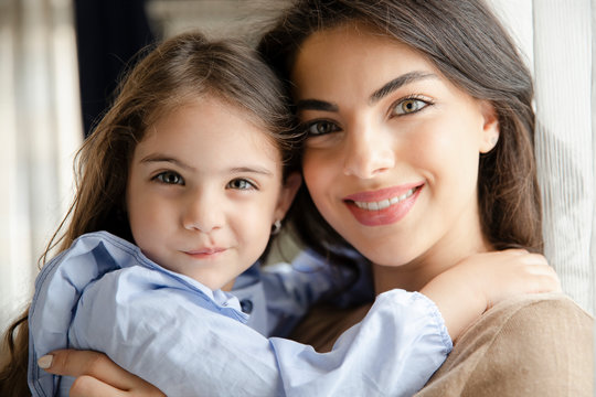 Beautiful young woman and her charming little daughter are hugging and smiling. Mother’s day concept. Little girl with mommy.