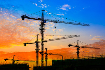 Tower crane and building construction site silhouette at sunrise.
