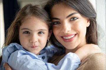 Beautiful young woman and her charming little daughter are hugging and smiling. Mother’s day concept.