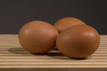 Three brown chicken eggs black background, close up.