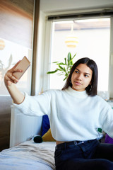 Urban fashion young girl holding cellphone and sitting on bed.