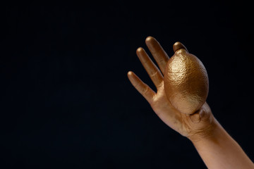 Hand holds lemon. Gold paint on black background