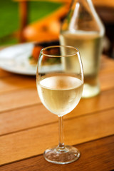 glass of white whine with condensation water drops bottle and meal in the background