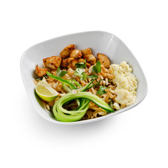 Fried udon noodles in a wok with pieces of pork. Served with tofu cheese, fresh cucumber and lime. Traditional asian food. Isolated on a white background.