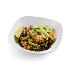 Fried udon noodles in a wok with mushrooms, fresh cucumber and cashew. Traditional asian food. Isolated on a white background.