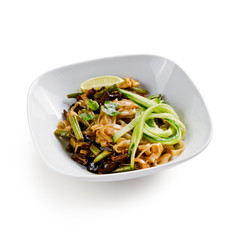 Fried udon noodles in a wok with mushrooms, fresh cucumber and cashew. Traditional asian food. Isolated on a white background.