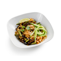 Fried udon noodles in a wok with mushrooms, fresh cucumber and cashew. Traditional asian food. Isolated on a white background.