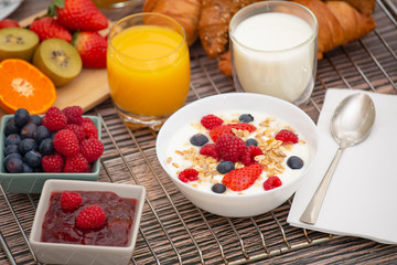 Breakfast Served in the morning with Fruit Yogurt, Butter croissant and corn flakes Whole grains and raisins with milk in cups and Strawberry, Raspberry, Kiwi, Fresh Orange Juice on breakfast table