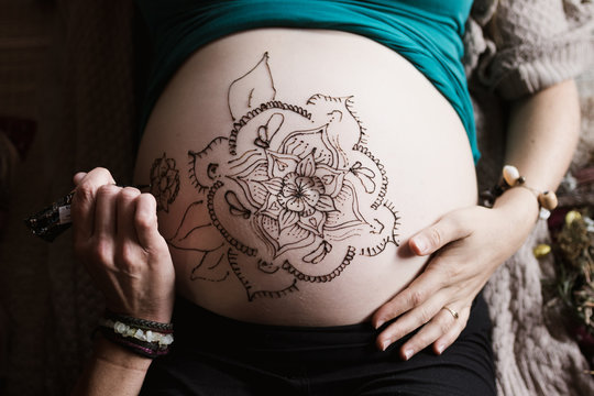 woman drawing Mehndi design on pregnant belly. Selective focus on belly.