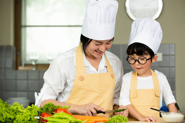 Happy  Asian  mother  with  son in chef  hat  cooking  salad in kitchen at home
