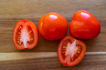 Two whole tomato and two halves of tomato are laying on a wooden cutting board, closeup view