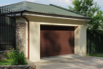 one concrete garage with closed brown gates under a green tiled roof outside on a sunny day