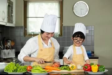Happy  Asian  mother  with  son in chef  hat  cooking  salad in kitchen at home