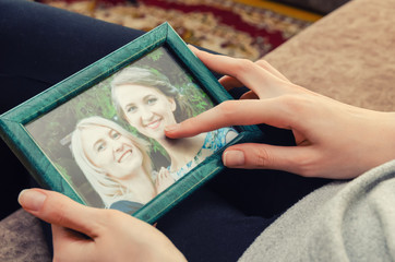 girl's hands hold a photo frame with a photo of two girls blonde and brown haired close up