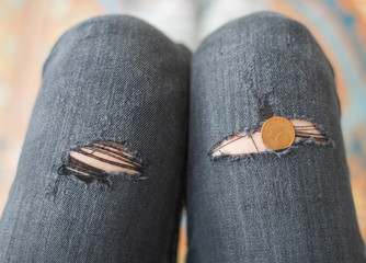 Knees in ripped jeans and a coin. Concept of economic crisis and unemployment