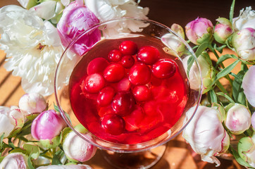 Magic solemn still life with glass of red drink with autumn organic berries surrounded by white flowers in the diagonal striped shadow of the blinds on a bright sunny day. Greeting card close-up