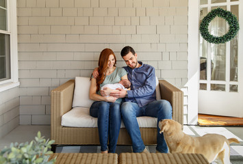 Happy first time parents holding newborn baby in their home. Dog meeting newborn baby.