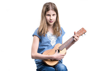 Young, blond girl in blue T-shirt is playing concert on ukulele instrument.