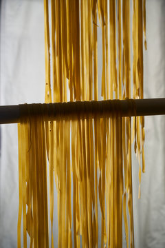two rows of fresh fettuccine pasta egg noodles hanging on rods to dry