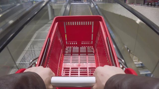 Point of view 4K slowmotion footage of hands with empty plastic red shopping cart moving on moving walkway in supermarket