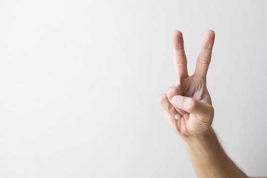 closeup hand indicating peace victory sign on white brick wall background