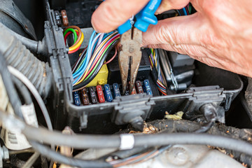 Mechanic with pliers checking the car fuse box of electric car