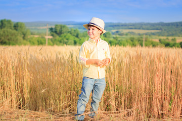 Naklejka na ściany i meble A boy in a straw hat stands near a yellow wheat field, looks away, smiles.