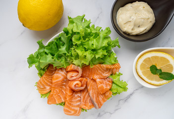 Raw salmon slice or salmon sashimi with green oak salad, lemon and white sauce in Japanese style  on white marble background. top view