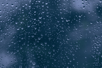 Naklejka na ściany i meble Close up of water rain droplet on a dark blue glass dripped window. big rainy drop on a window pane during a shower stormy weather. rainy season in the city.