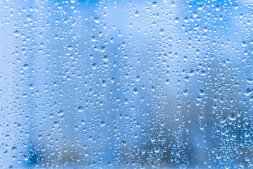 Naklejka na ściany i meble Close-up of water droplets on a light blue running down on glass transparent surface. rainy drops on a window pane during a summer shower stormy weather. rainy season.