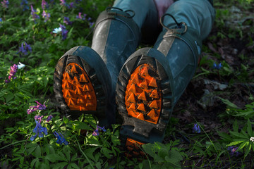 legs in special rubber boots with an orange sole lie in spring grass with flowers in the forest for...