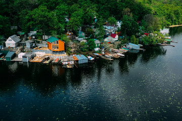 Fototapeta na wymiar Russian fishing village with colored wooden houses and boats in a green oak forest on the river bank