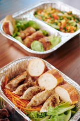 Foil tray with ready meal of gyoza or dumplings, carrot and white bread on kitchen table