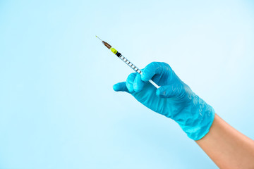 Hand in blue glove holding a plastic syringe with liquid for injection on light blue background. Health care, treatment concep