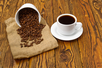 White coffee cup with aromatic coffee drink on brown wooden table. Coffee seeds on antique wooden table with mug of coffee drink