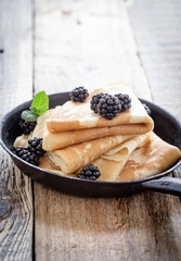 Pan of crepes with fresh blackberries on wooden table
