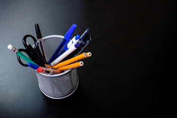 Metal stand with pencils, pens, scissors on wooden table