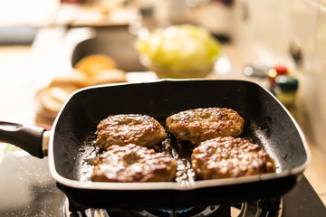 pork burgers fried in hot pan on strove in kitchen