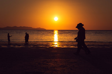 Fototapeta premium people walking on beach at sunset