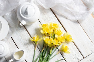 Flay lay on fresh narcissus on white wooden table with tea set