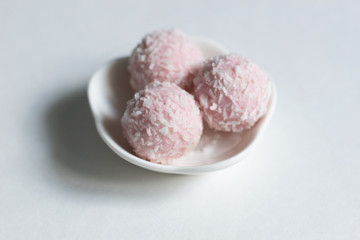 Pink raspberry sweet energy balls with coconut flakes in bowl on white background