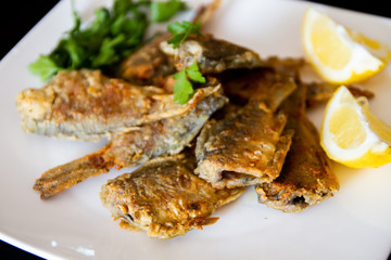 Fried fish on a white plate. Grilled crucian with lemon and parsley.