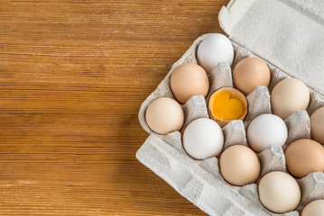 tray cardboard with chicken eggs one egg is broken visible yolk.