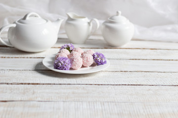 Pink sweet energy balls with coconut flakes, primula flowers in plate, tea crockery  on white wooden background