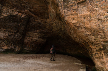 Male tourist examines a large cave in Sigulda (Latvia), the walls of which are covered with inscriptions of different years