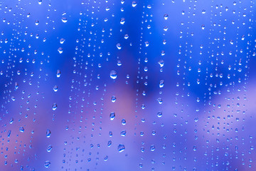Fototapeta na wymiar blue rain water drops on a window glass close up , colored drop macro in a blue light