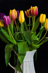 A still life with a bouquet of colourful tulips in a white vase in front of black background